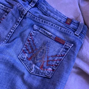 Lågmidjade 2000- talet jeans  - Snygga blå jeans med unikt broderi i rött och blått på bakfickorna. De har en klassisk femficksdesign och knappgylf. Perfekta för en avslappnad stil. Nypris: 2000 kr 