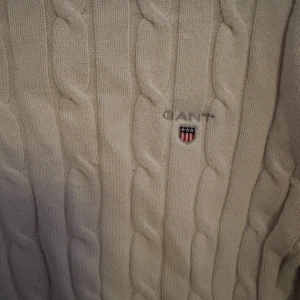 Beige kabelstickad tröja från GANT - Säljer en stilren vit kabelstickad tröja från GANT. Tröjan har en klassisk rund halsringning och långa ärmar. Perfekt för en elegant och avslappnad look.