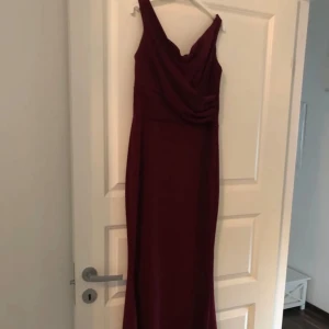 Vinröd aftonklänning - Elegant vinröd långklänning med draperad detalj framtill. Klänningen har en smickrande passform och är perfekt för festliga tillfällen.