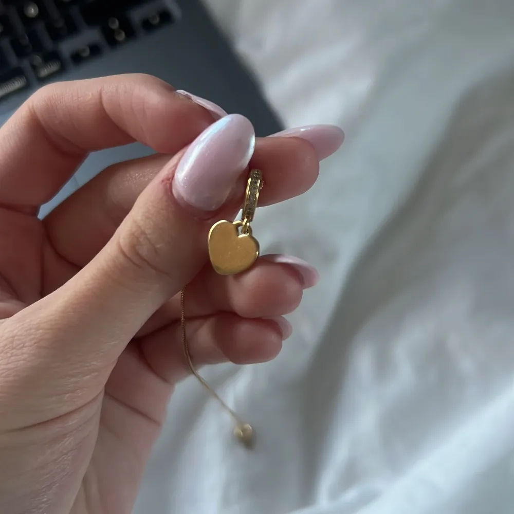 Elegant guldhalsband med ett litet hjärthänge. Perfekt för att lägga till en subtil touch av kärlek och stil till din outfit. Kedjan är tunn och smidig, brickan har inget inskrivet på sig . Asusteet.