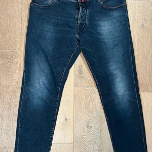 Mörkblå jeans från Jacob Cohen - Snygga mörkblå jeans från Jacob Cohen med kontrasterande sömmar och klassisk femficksdesign. Byxorna har en knappgylf och en diskret logotyp på baksidan. Perfekta för en stilren look.