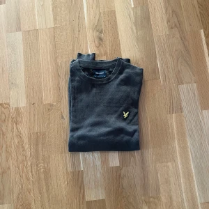 Mörkgrön tröja från Lyle & Scott - Säljer en stilren grå tröja från Lyle & Scott med deras ikoniska logga på bröstet. Perfekt för en avslappnad och snygg look.