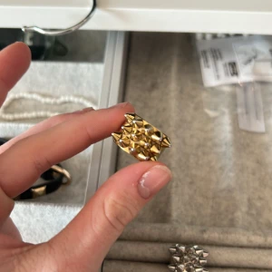 Guldfärgad ring med nitar - Snygg guldfärgad ring med nitar som ger en edgy look. Perfekt för att addera lite attityd till din stil. Ringen har en unik design med spetsiga detaljer. Har tappat lite färg 