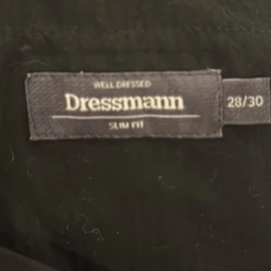 Svart kostymbyxa och kavaj från Dressmann - Snygg svart kostym från Dressmann i slim fit. Perfekta för en stilren look. Byxorna har en klassisk design med knapp och dragkedja framtill. Vi har två olika storlekar på byxorna men bara en size till kavajen säljer sättet för 1000 eller byxa för sig själv 500