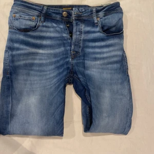 Blå jeans från Jack & Jones - Snygga blå jeans från Jack & Jones med en klassisk femficksdesign. De har en knappgylf och en läderpatch med logotyp baktill. Perfekta för en avslappnad stil. 41cm tvärsöver midjan, 18cm nere vid fötterna, längd på jeansen är 101cm