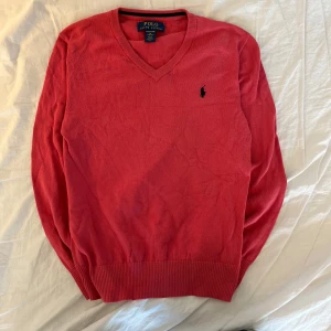 Röd tröja från Polo Ralph Lauren - Säljer en snygg röd tröja från Polo Ralph Lauren i mjuk bomull. Tröjan har en klassisk v-ringning och det ikoniska logotypbroderiet på bröstet. Perfekt för en stilren look. Medela vid minsta fundering