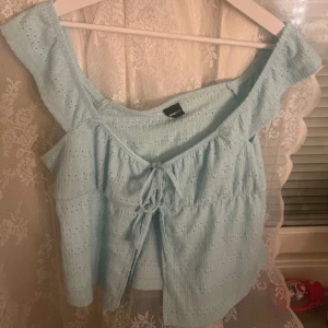 Ljusblå topp från Gina Tricot - Söt ljusblå topp från Gina Tricot med knytning framtill. Toppen har ett hålmönster och är perfekt för varma sommardagar. Den är luftig och ger en romantisk känsla.