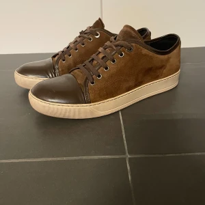  sneakers från Lanvin - Snygga bruna sneakers från Lanvin med en kombination av mocka och skinn. Skorna har en klassisk snörning och en ljus sula som ger en stilren look. Skorna är i väldigt bra skick. Nypris: ca: 4500kr. Mitt pris: ca 1300. En defekt: sönder snöre men är billig att att byta o köpa nya därav priset.