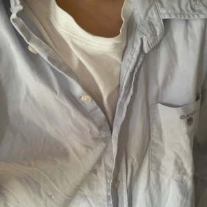 Ljusblå skjorta från GANT - Säljer en klassisk ljusblå skjorta från GANT med bröstficka och broderad logga. Skjortan har långa ärmar och knappar framtill. Perfekt för en stilren look. Passar helt perfekt inför sommaren🍾🍾