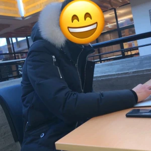 Svart dunjacka från Moose Knuckles - Säljer en snygg svart dunjacka från Moose Knuckles med vit pälskant på huvan. Jackan har flera dragkedjor och knappar, samt en cool logga på ärmen. Perfekt för kalla dagar!