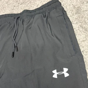 Under Armour Träningsbyxor - Träningsbyxor från Under Armour med en fluorescerande reflekterande logga som ger synlighet vid träning i mörka förhållanden. Byxorna är designade för att ge bra rörelsefrihet och komfort, och de är tillverkade i slitstarka material. Perfekta för både inomhus- och utomhusaktiviteter. Storlek S, helt oanvända. 