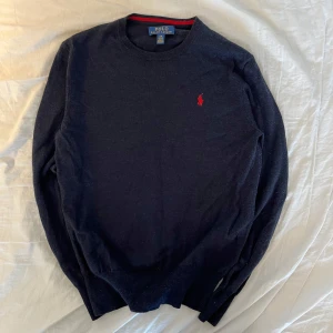 Polo stickad tröja - Säljer en stilren mörkblå tröja från Polo Ralph Lauren i 100% extra fin merinoull. Tröjan har en klassisk design med rund hals och ett rött broderat märke på bröstet. Perfekt för kyligare dagar. Säljer då jag inte passar i den längre, medela vid minsta funderingar! 👍