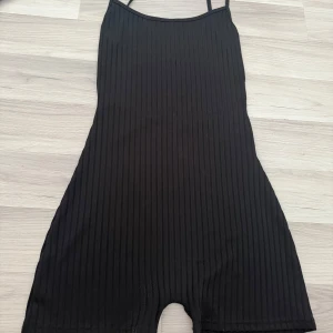 Svart ribbad jumpsuit  - Snygg svart ribbad jumpsuit med smala axelband. Perfekt för en stilren look. Tillverkad i ett stretchigt material som ger en bekväm passform.