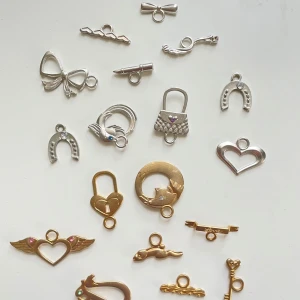 Blandade berlocker  - Säljer ett set med olika berlocker i både guld och silver. Inkluderar motiv som hjärtan, hästskor, nycklar och rosetter. Perfekt för att skapa personliga smycken eller som dekorationer.