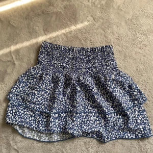 Blommig kjol från Emery Rose - Söt blå och vit blommig kjol från Emery Rose. Kjolen har en volangdetalj och en elastisk midja för en bekväm passform. Perfekt för en somrig look!