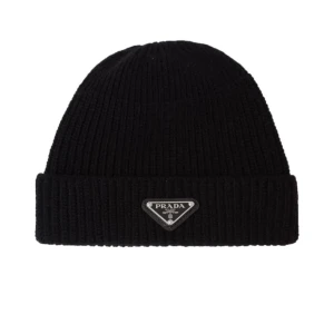 Svart ribbad mössa från Prada - Snygg svart ribbad mössa från Prada med deras ikoniska logotyp framtill. Perfekt för att hålla värmen med stil under kyliga dagar.
