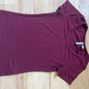 Vinröd t-shirt från hm - Säljer en stilren vinröd t-shirt från Divided. Den har en klassisk rund hals och korta ärmar, perfekt för en avslappnad look. Materialet känns mjukt och bekvämt mot huden. Passar perfekt till jeans eller kjol för en enkel vardagsstil.