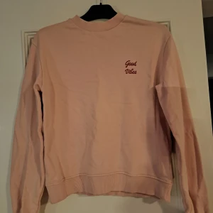 Rosa tröja från NA-KD - Säljer en söt rosa tröja från NA-KD med texten 'Good Vibes' broderad på bröstet. Tröjan har långa ärmar och ribbade muddar vid ärmslut och nederkant. Perfekt för en avslappnad stil.