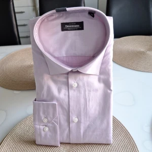 Ljusrosa skjorta från Dressmann - Säljer en stilren ljusrosa skjorta från Dressmann i premium bomull. Skjortan har en klassisk krage och knappar framtill. Perfekt för en elegant look.