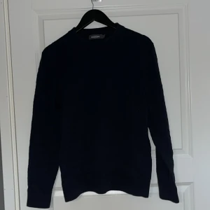 Mörkblå stickad tröja från Dressman - Säljer en stilren mörkblå stickad tröja från Dressman. Tröjan har ett diskret mönster och långa ärmar, perfekt för kyligare dagar. Den är mjuk och bekväm, idealisk för både vardag och mer uppklädda tillfällen.