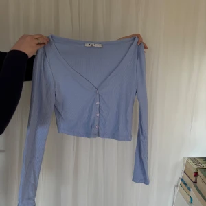 Ljusblå ribbad kofta - Säljer en ljusblå ribbad kofta från NA-KD. Den har en v-ringad design med knappar framtill och långa ärmar. Perfekt för lager-på-lager-stil eller som ett lättare plagg under vår och sommar. 🌸