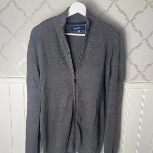 Grå stickad tröja från Blend - Säljer en stilren grå stickad tröja från Blend med dragkedja framtill. Den är tunn och perfekt för sommaren men har även en ribbad krage och långa ärmar, perfekt för kyligare dagar. Hör av er vid frågor angående mått osv!