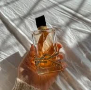 Parfym med elegant design - En lyxig parfymflaska med en rektangulär form och en svart kork. Flaskan har en gyllene vätska inuti och ett stilrent metallband som dekoration. Perfekt för den som vill ha en sofistikerad doftupplevelse.