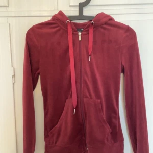 Röd velourkofta med dragkedja - Snygg röd velourkofta med dragkedja och huva. Jackan har långa ärmar och praktiska fickor framtill. Perfekt för en avslappnad stil.