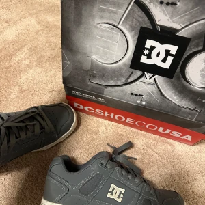 Grå sneakers från DC Shoes - Snygga grå sneakers från DC Shoes med klassisk design och logotyp på sidan. Skorna har snörning och en vit sula med bruna detaljer. Perfekta för en avslappnad stil. Pris kan diskuteras, använt flera gånger 