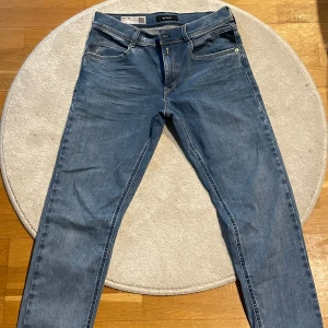 Blå jeans från Replay - Snygga blå jeans från Replay med klassisk femficksdesign och dragkjedjsgylf. Perfekta för en avslappnad stil. Märkesdetaljer syns på baksidan och insidan av midjan. Barn storlek 164