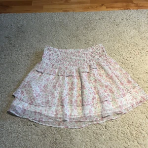 Blommig kjol från Gina Tricot - Söt blommig kjol från Gina Tricot i rosa och gröna nyanser. Kjolen har en elastisk midja och volangdetaljer som ger en lekfull look. Perfekt för varma dagar! Inte använd alls många gånger men är väldigt elastisk. Skriv gärna frågor om ni undrar något :)