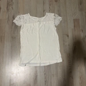 Vit blus med spetsdetaljer - Säljer en söt vit blus med korta spetsärmar. Perfekt för en somrig look eller en avslappnad dag. Blusen har en enkel och stilren design med vackra spetsdetaljer vid ärmarna.