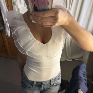 Vit topp med volangdetaljer - Jättefin och unik body! Använd en gång men har en liten fläck på magen, syns knappt. (Har samma i svart om någon är intresserad) 🤗