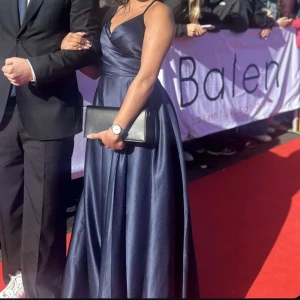 Mörkblå långklänning - Elegant mörkblå långklänning med omlott-design och smala axelband. Klänningen har en v-ringad urringning och en stilren siluett som passar perfekt för formella tillfällen. Köpt för 1800, och är använd en gång. Pris går att diskutera!