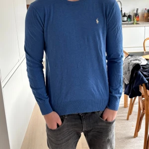 Blå tröja från Ralph Lauren - Säljer en stilren blå tröja från Ralph Lauren med det klassiska logotypbroderiet på bröstet. Tröjan har långa ärmar och ribbade muddar vid ärmslut och nederkant. Perfekt för en avslappnad men snygg look.