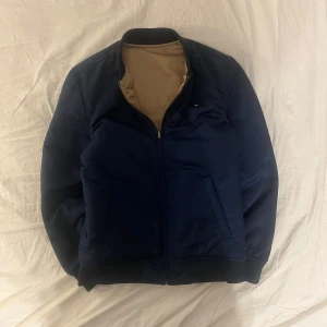Vändbar bomberjacka från Tommy Hilfiger - Säljer denna riktigt feta vändbara bomberjacka från Tommy Hilfiger i marinblått och beige. Jackan har dragkedja och ribbade muddar. Perfekt för att variera din stil med två färger i en jacka. Denna jacka är parfekt nu för våren! Skriv vid minsta funderingar! 👍