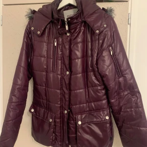 Lila quiltad jacka från Esmara - Säljer en snygg mörk lila quiltad jacka från Esmara. Jackan har en avtagbar huva med fuskpäls och praktiska fickor med knappar. Den är långärmad och har dragkedja framtill. Perfekt för kyliga dagar! Vattentät. Oanvänd. 