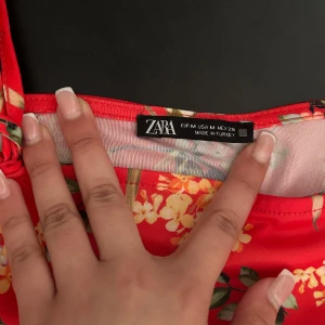 Röd blommig topp från Zara - Säljer en färgglad röd topp från Zara med ett vackert blommönster i olika nyanser, perfekt inför sommaren ;). Toppen har smala axelband som man kan skjustera själv.🌺🌺