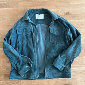 Grön manchesterjacka från These Glory Days - Snygg grön manchesterjacka från These Glory Days med dragkedja framtill. Jackan har långa ärmar och två bröstfickor. Perfekt för en stilren look. Cond 9/10 