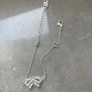 Silverarmband med rosett Lily & Rose - Elegant silverarmband med en glittrig rosett som detalj. Armbandet har en justerbar kedja och ett smidigt lås. Perfekt för att lägga till en touch av glamour till din outfit.