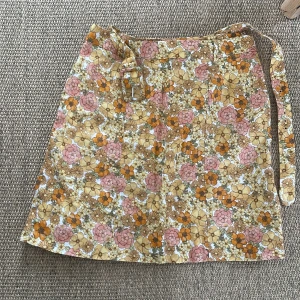 Blommig kjol från & Other Stories - Säljer en superfin blommig kjol från & Other Stories. Kjolen har ett härligt mönster i rosa, orange och beige toner. Den har en dragkedja på sidan och ett matchande bälte för en snygg passform. Perfekt för vår och sommar! 🌸