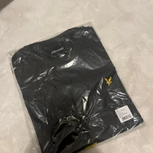 Mörkgrå t-shirt från Lyle & Scott - Helt ny mörkgrå t-shirt (charcoal mark) från Lyle & Scott. Prislappen är kvar och den ligger kvar i påsen, inte ens testad. Nypris är 399kr. 