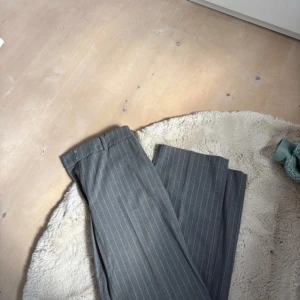 kostymbyxor - Snygga grå kostymbyxor med diskreta vita ränder. Byxorna har en klassisk passform och är perfekta för en stilren look. De är tillverkade i ett bekvämt material som ger en elegant känsla. Helt nya!