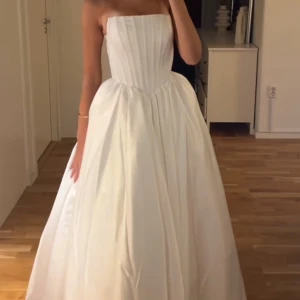 Vit bal/bröllopklänning - Elegant vit axelbandslös långklänning med snörning i ryggen. Klänningen har en klassisk och tidlös design med en vacker voluminös kjol. Perfekt för speciella tillfällen.