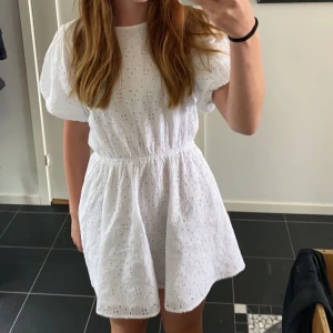 Vit klänning med broderad spets - Charmig vit klänning med broderad spets och korta ärmar. Har en rosett i ryggen men tyvärr ingen bild men den då den är för liten för mig. Perfekt för sommarens alla tillfällen. Den har en elastisk midja som ger en smickrande passform. Prislappen är kvar