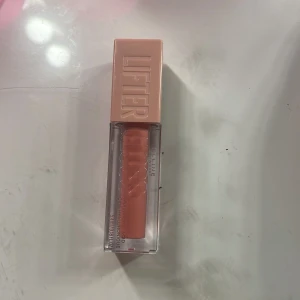 Läppglans från Maybelline - Snyggt läppglans från Maybelline med en ljusrosa nyans. Förpackningen är stilren med en fyrkantig design och ett lock i matchande färg. Perfekt för att ge läpparna en glansig finish. Oanvänd