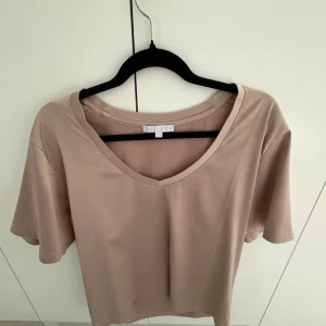 Beige t-shirt från Blond Hour - Säljer en stilren beige t-shirt från Blond Hour. Den har en v-ringad hals och korta ärmar, perfekt för en avslappnad look. Materialet känns mjukt och bekvämt mot huden.
