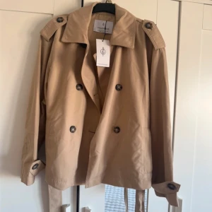 Kort trenchcoat med bälte  - Supersnygg kort trenchcoat med bälte från stradivarius! Storlek xs, ny med lappar