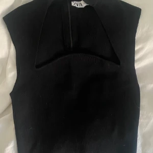 Svart topp från Zara - Snygg svart topp från Zara med en unik design. Toppen har en v-ringad detalj och är ärmlös, vilket ger en stilren look. Perfekt för att lägga till en touch av elegans till din outfit.