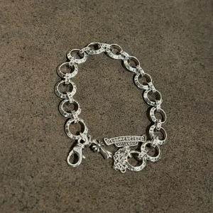 Rockstar Charm Bracelet - Stilfullt armband med rockig attityd, prydd med charmiga detaljer. 19,5 cm långt men kan enkelt justeras genom att fästa i ringarna för en kortare passform. Perfekt för den som vill ha en personlig och trendig look